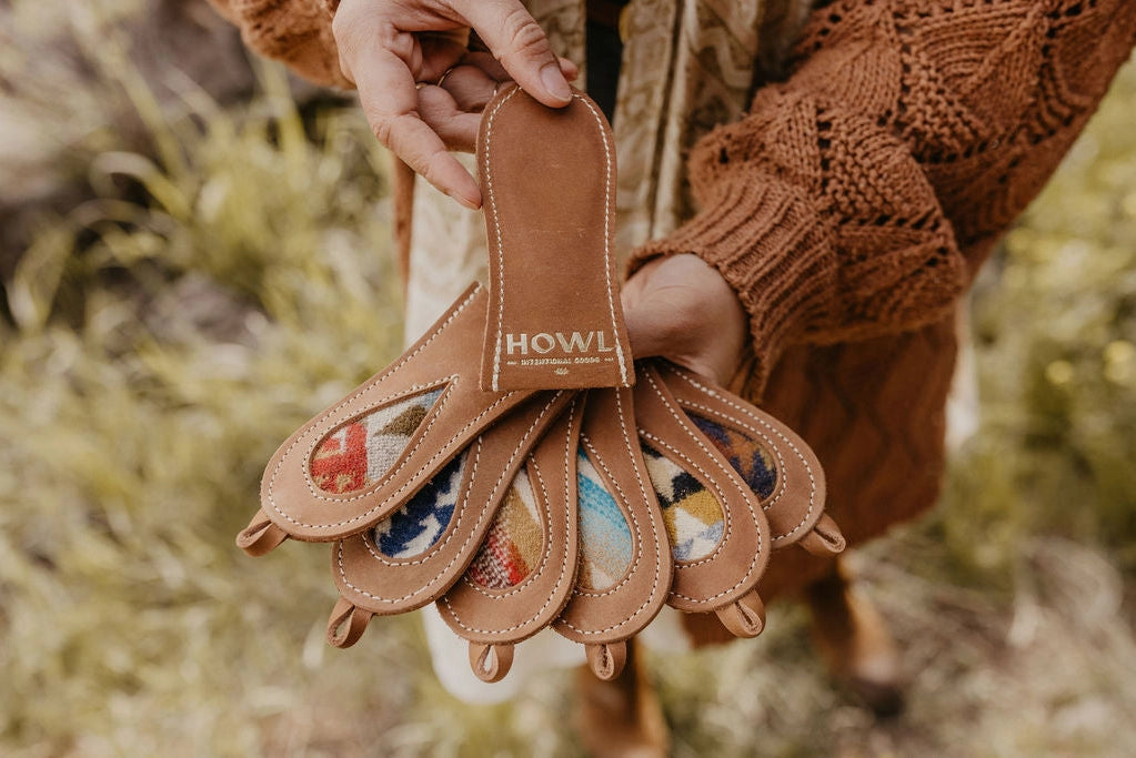 A person holding a brown leather cast iron handle with the brand name 'HOWL' embossed on it, with a blurred background suggesting an outdoor setting.