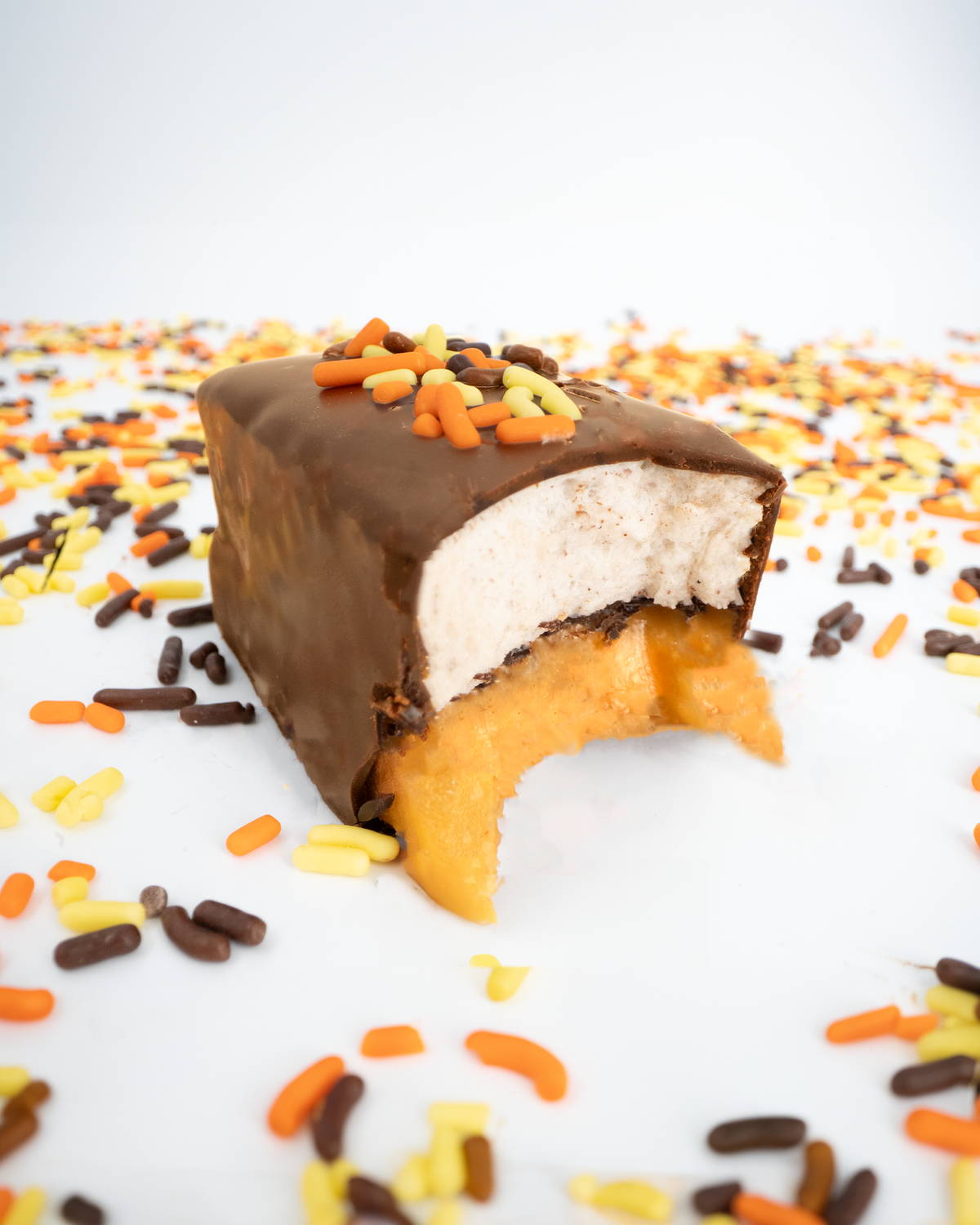 A bitten Pumpkin Spice Mini Bar with dark chocolate topping and multicolored sprinkles scattered around.