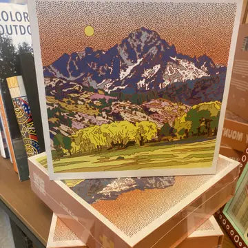 Art print puzzle of a mountain landscape with trees on a wooden surface.