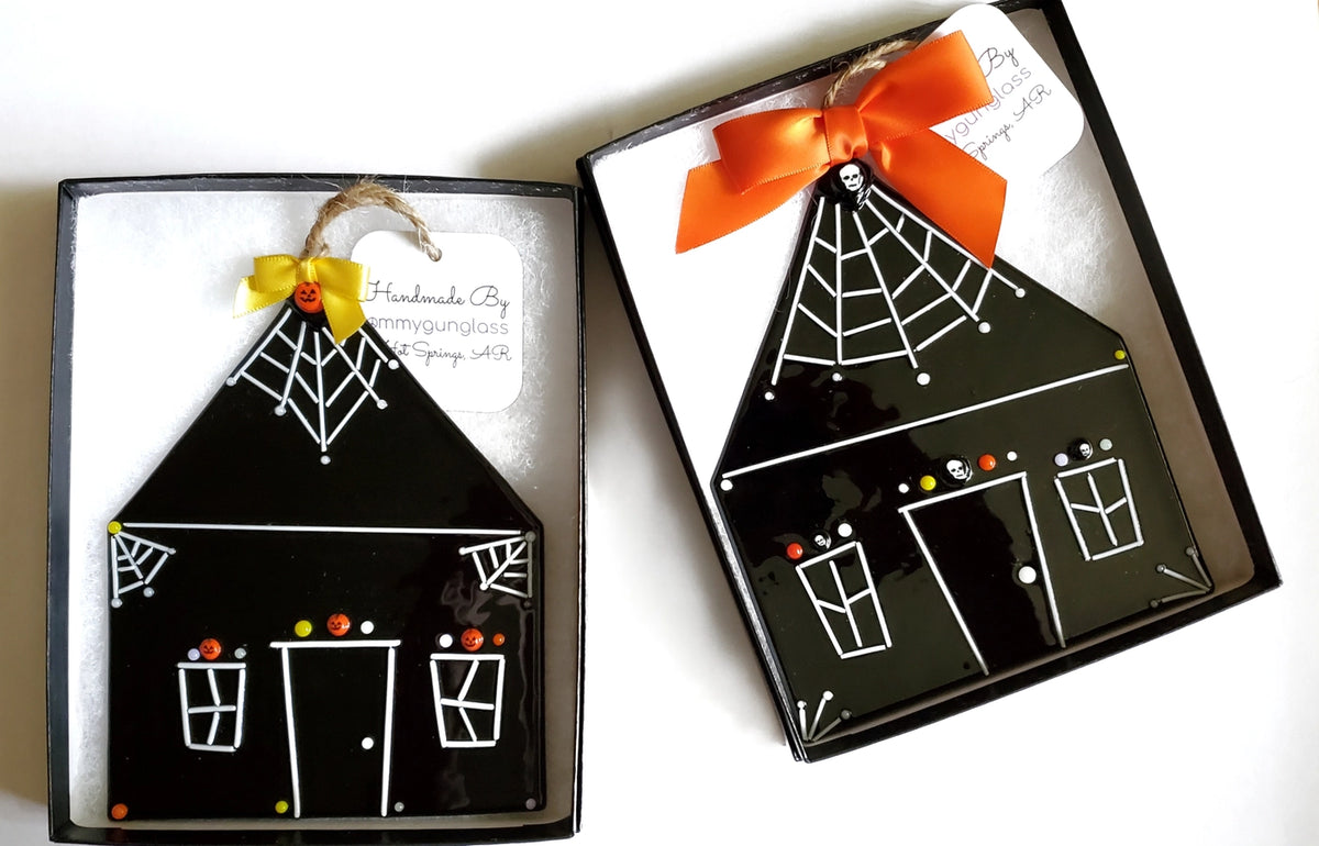 Halloween-themed house-shaped ornament with spider webs and a bow in a box.