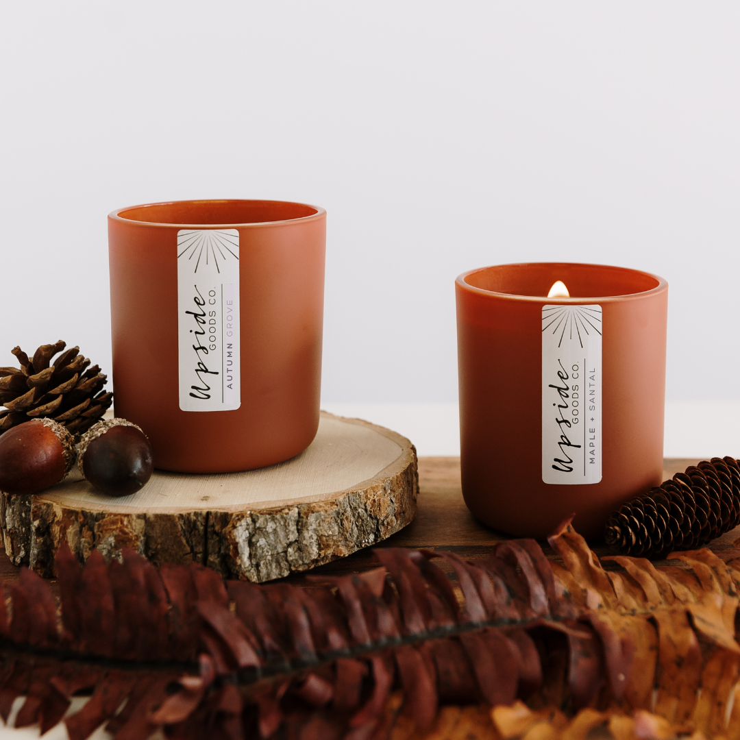 Two Upside Goods' Fall Candles in jars with pine cones, accorns, and leaves for decoration