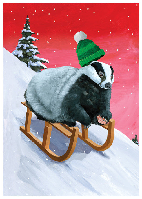 Illustrated Badger Sledding Downhill at Speed with a Hat flying off and a snowy pine tree make the front of this holiday card