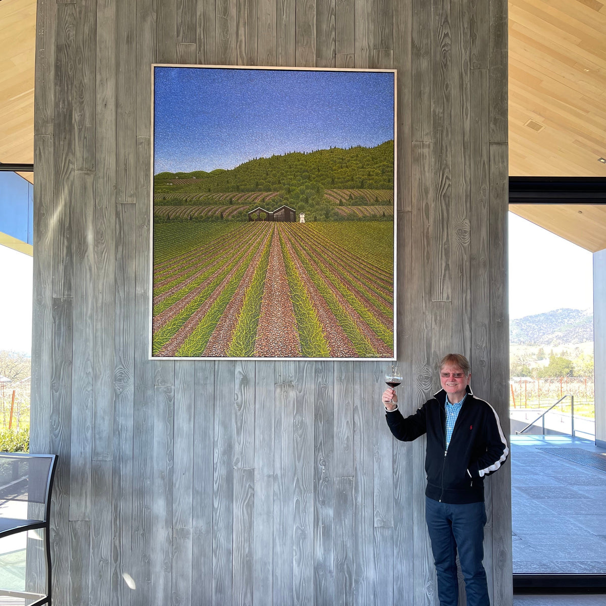 Father Arthur Poulin in Sonoma posed with a glass of wine in front of one of his pointilist original paintings