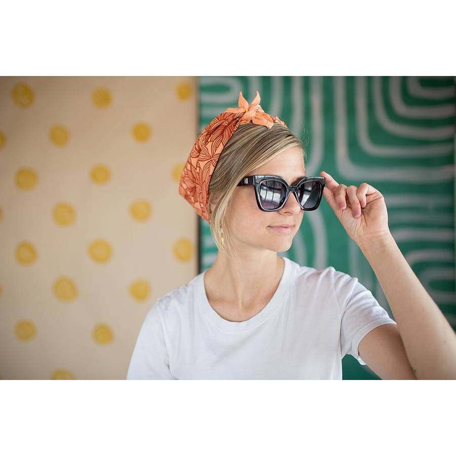 Young White Woman wearing a tied Hemlock Goods Orange Floral Bandana on her head and large black sunglasses