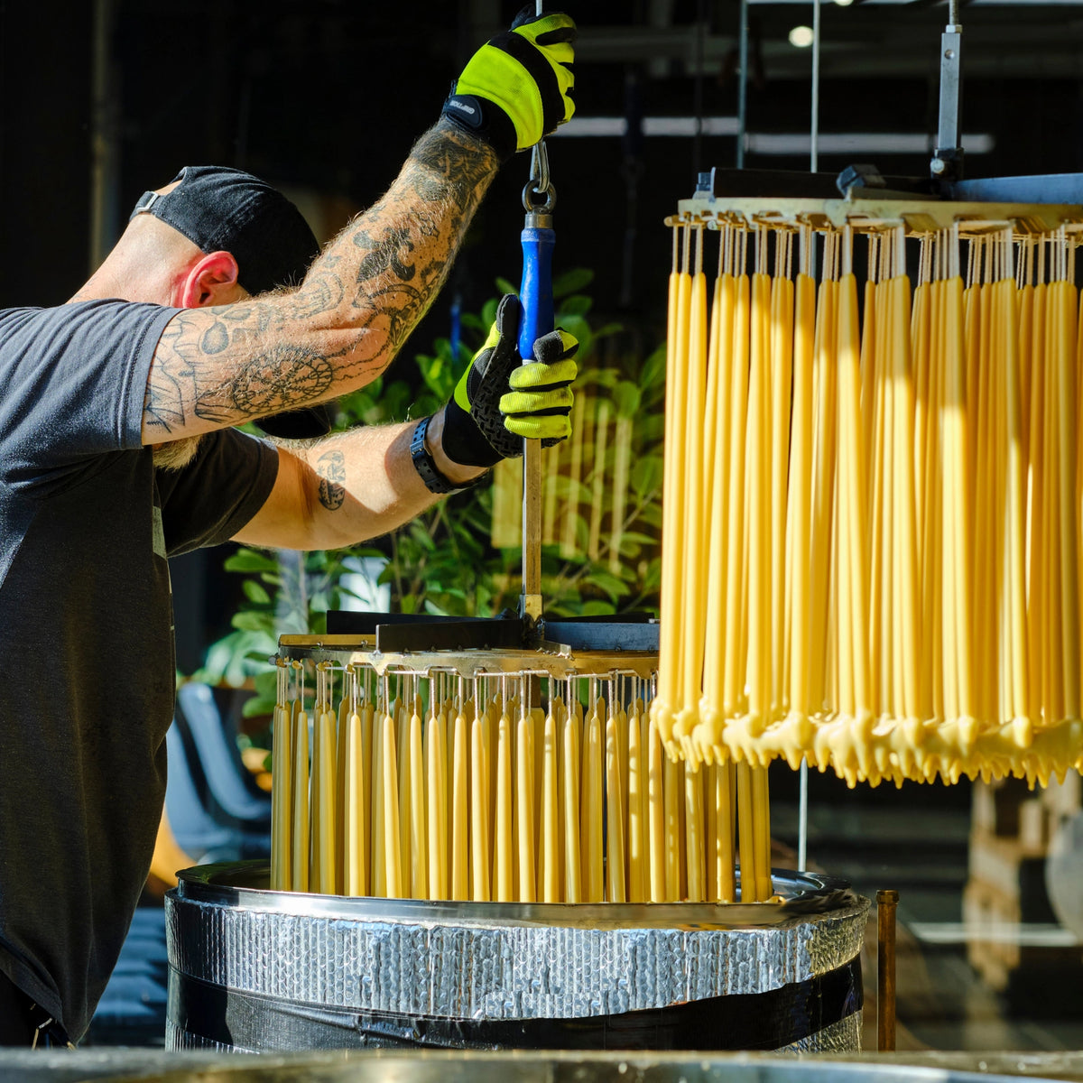 Person working with raw beeswax candles being dipped  on a machine in an industrial setting