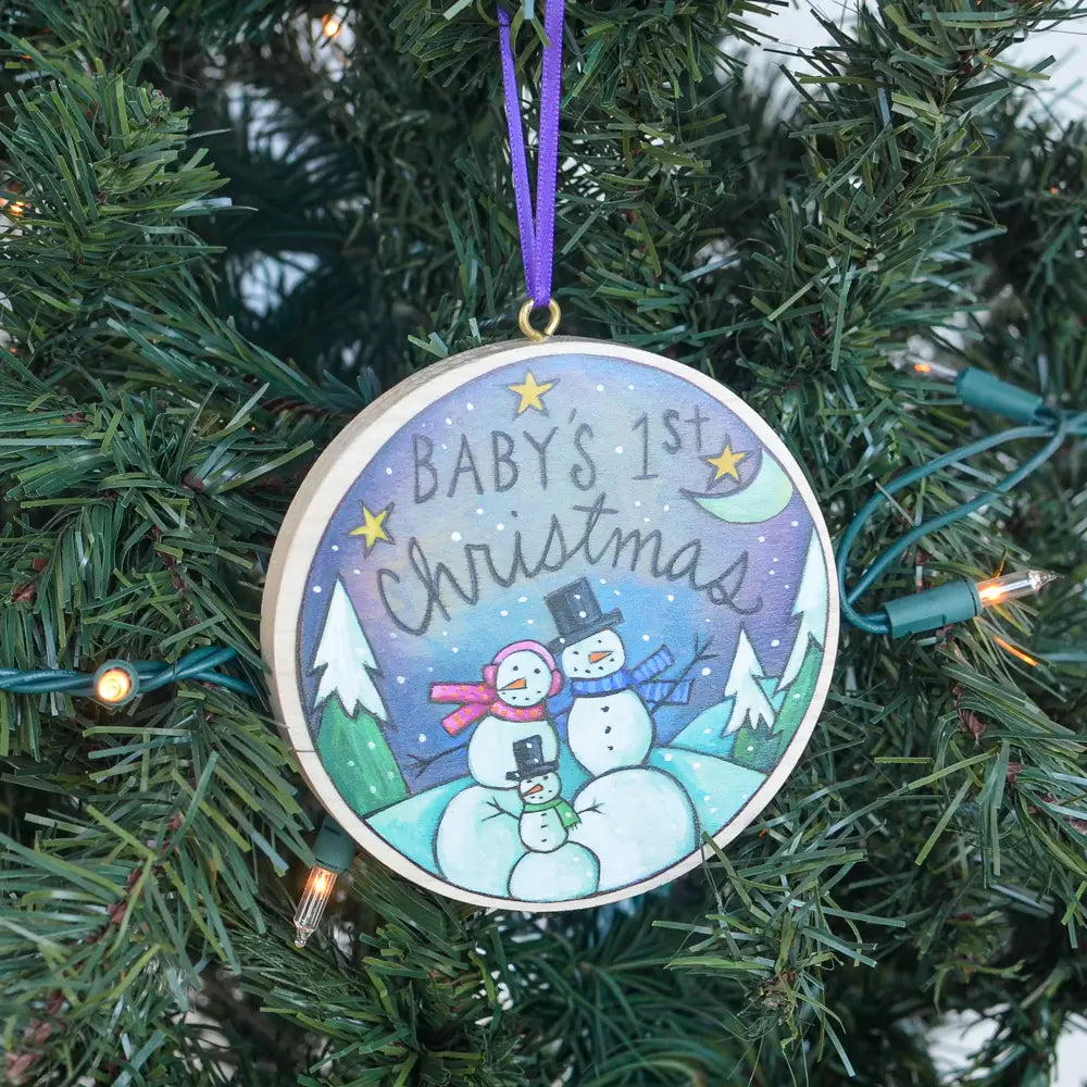 Decorative ornament for 'Baby's 1st Christmas' hanging on a Christmas tree.