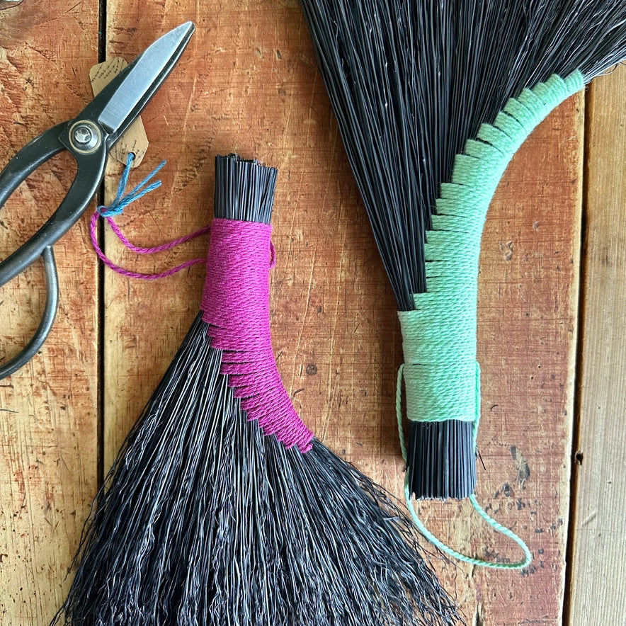 Two brooms with colorful handles and a pair of scissors on a wooden surface