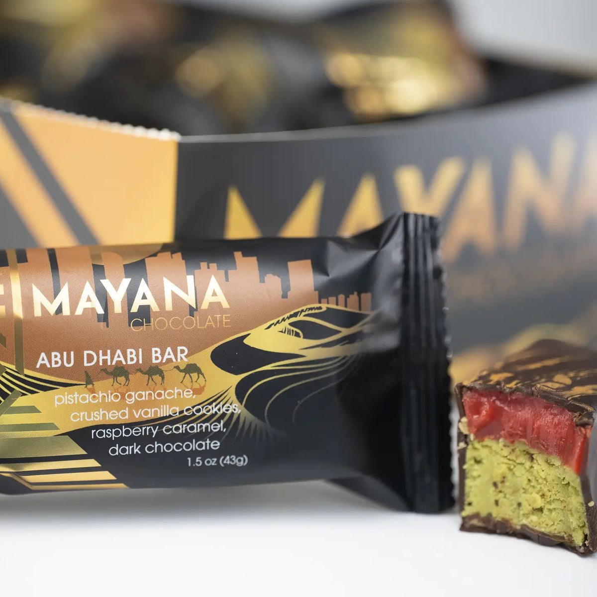 Mayana chocolate bar packaging with a close-up of the chocolate inside, set against a blurred background.