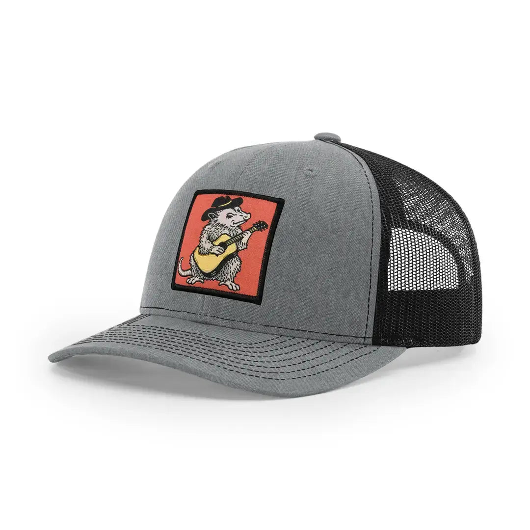 A gray and black trucker cap featuring a square patch on the front with a cartoon mouse playing a guitar on a red-orange background.