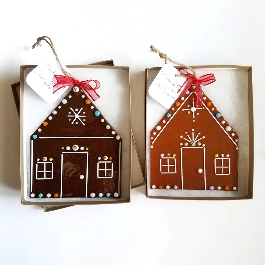 Two gingerbread house-shaped fused glass ornaments with decorative ribbons on a white background