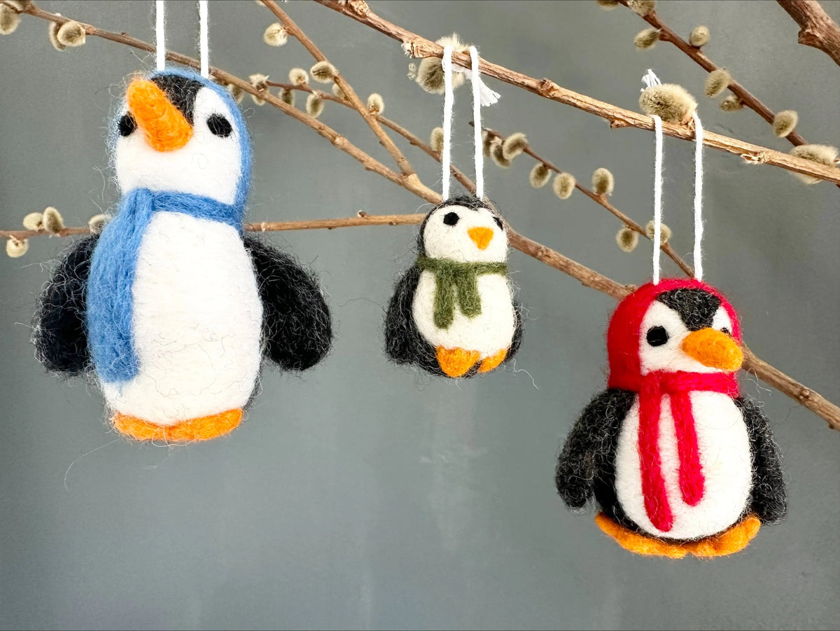 Three felted penguin ornaments with scarves hanging from a branch.