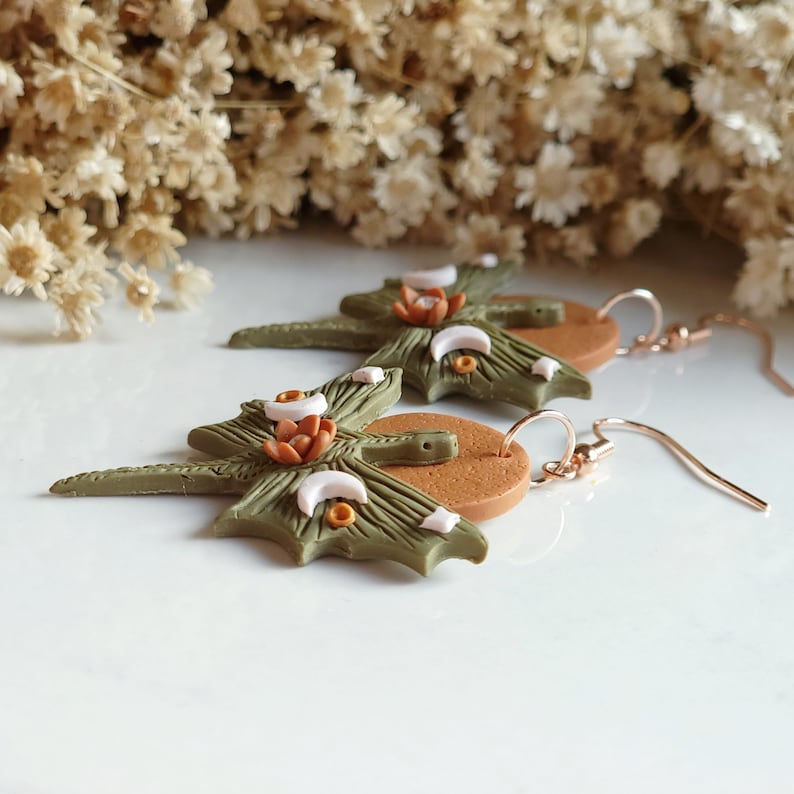 Pair of leaf-shaped earrings with a white background and dried flowers.