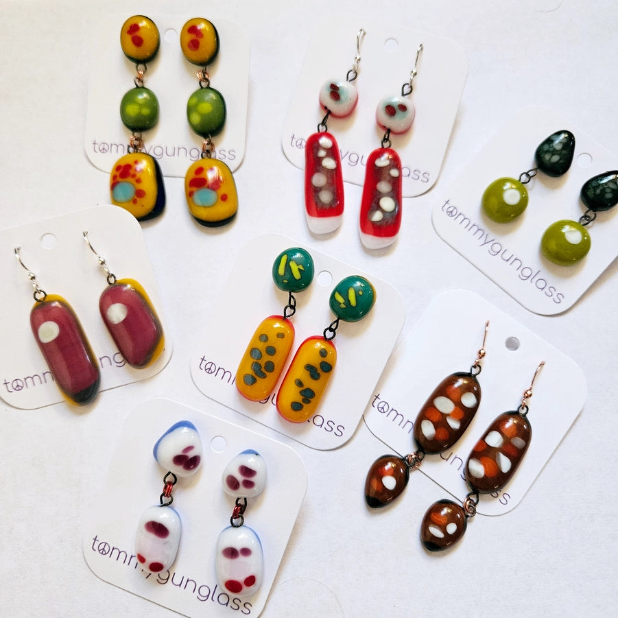 Colorful earrings on cards with 'tommygunglass' branding.