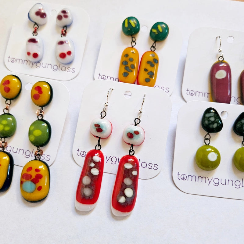 Colorful earrings on display with 'tommygunglass' branding