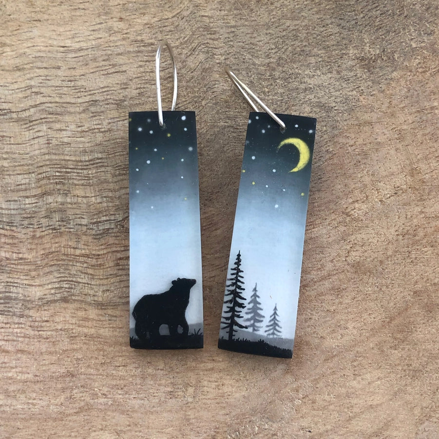 Pair of earrings with bear and tree design on a wooden surface