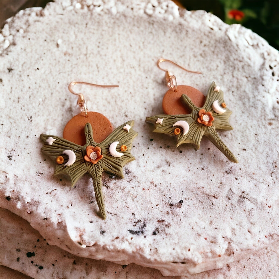 Pair of green leaf-shaped earrings with brown circular pendants on a textured white surface.