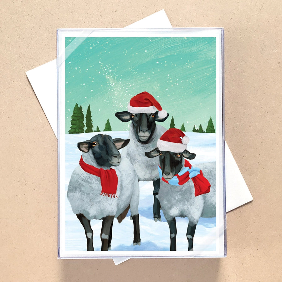 Christmas card with three sheep wearing Santa hats and scarves on a snowy background.