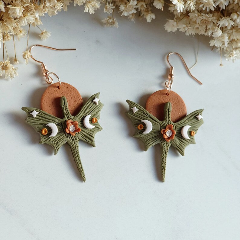 Pair of earrings with green leaf design and brown circular center on a light gray background.