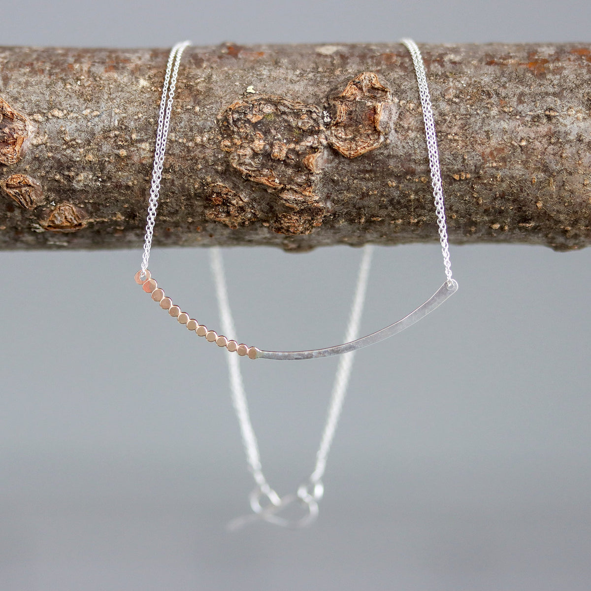 Silver necklace draped over a branch with a gray background