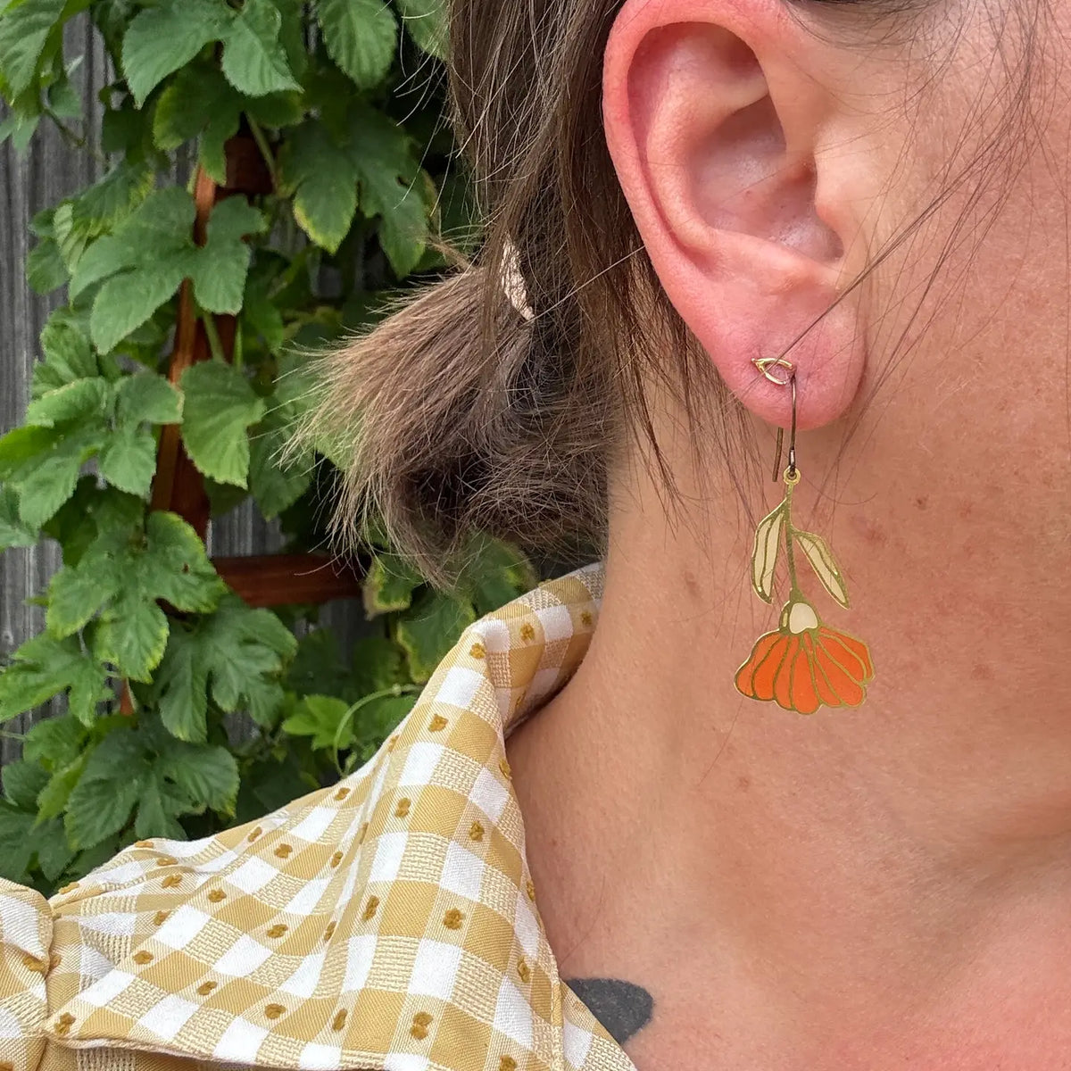 Close-up of a person wearing an orange floral earring with a green leafy background