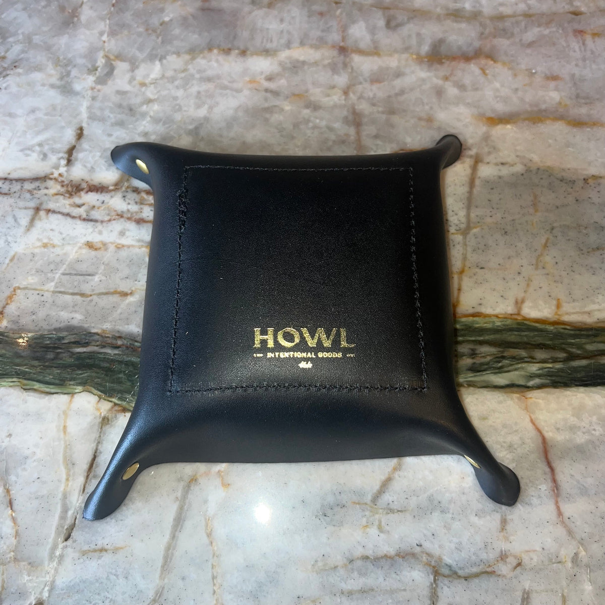 Black leather tray with 'HOWL' branding on a marble surface