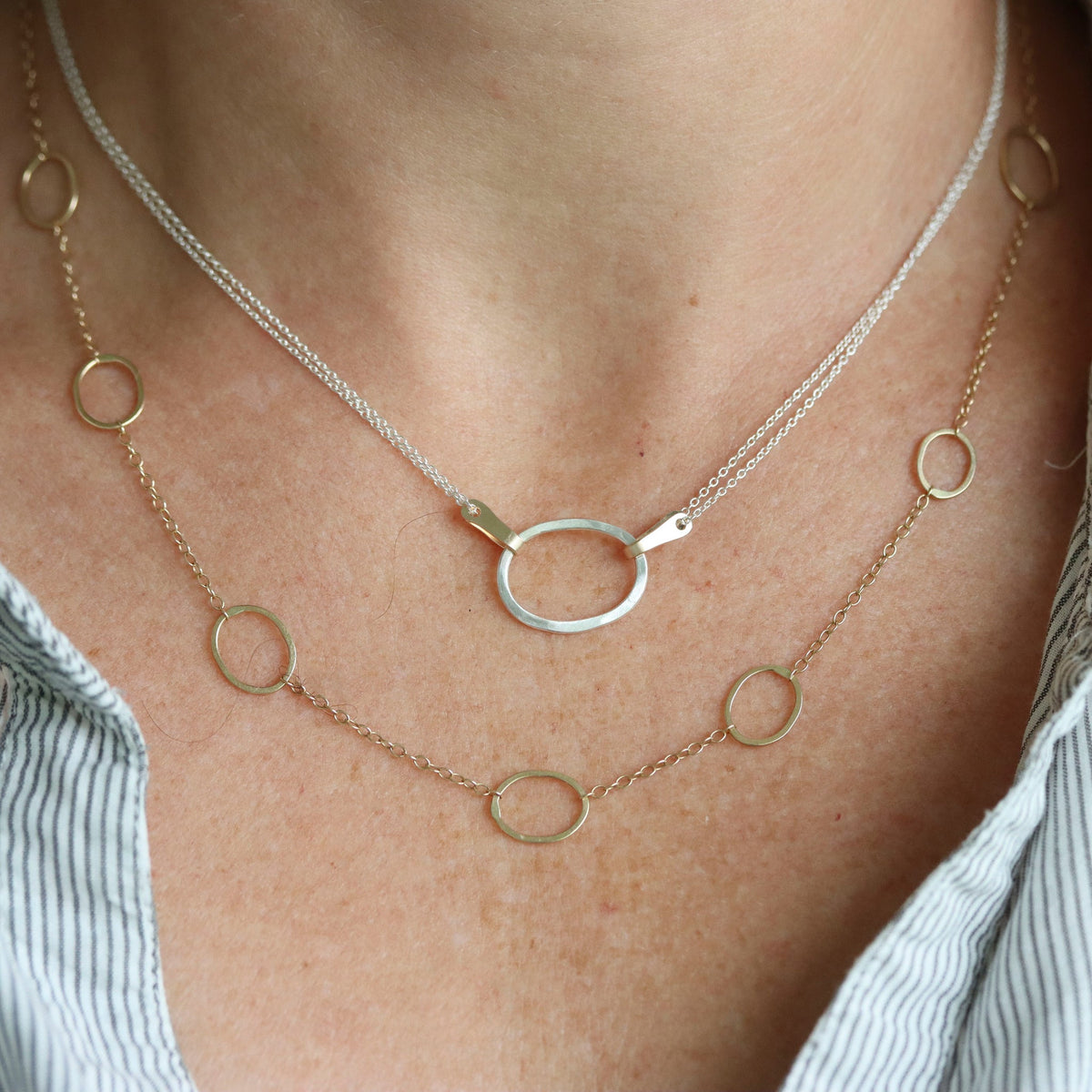 Close-up of a person wearing two necklaces with circular pendants on a plain background.