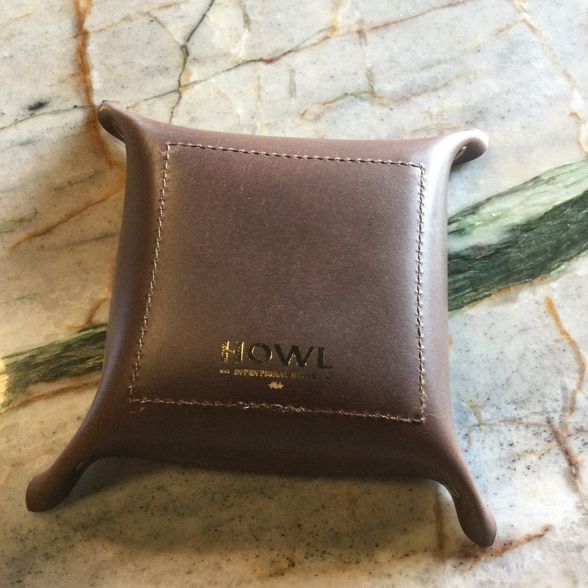 Brown leather jewelry display stand with 'HOWL' branding on a marble surface