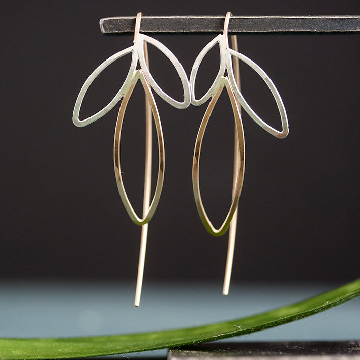 Pair of gold and silver earrings on a dark background with a green leaf.