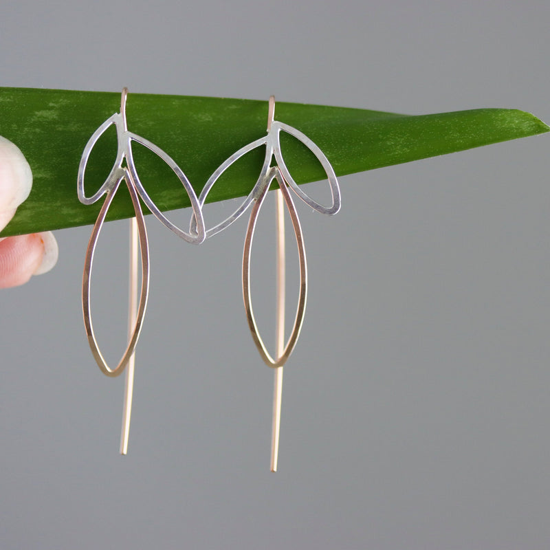 Pair of silver and gold earrings on a green leaf against a gray background