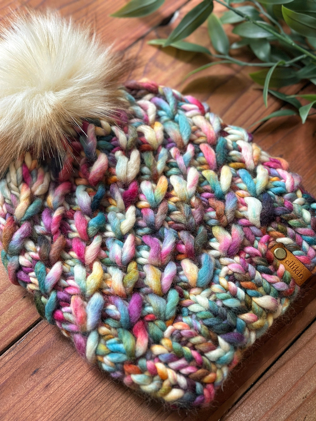 Multicolored knitted beanie with a fluffy pom-pom on a wooden surface.