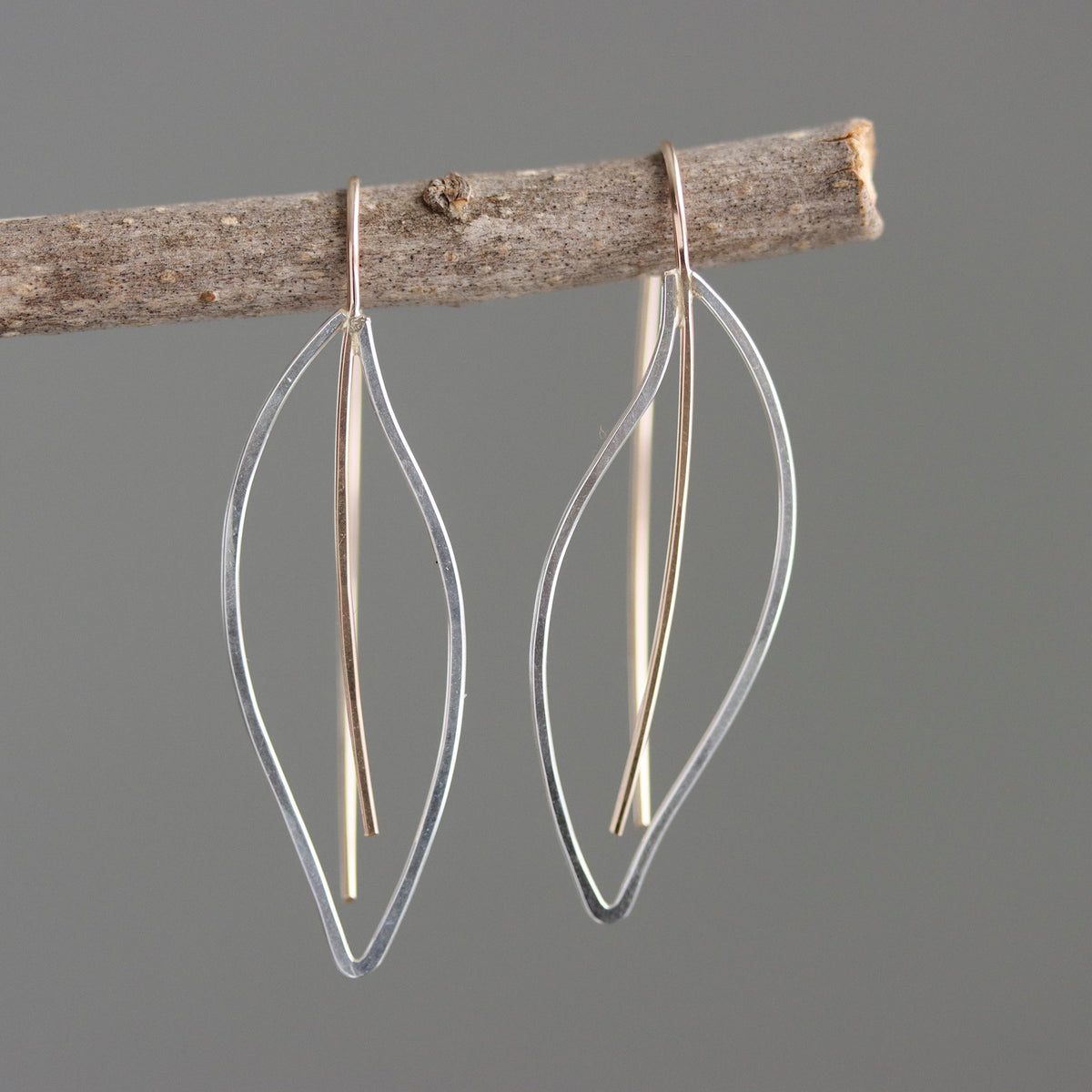 Pair of leaf-shaped earrings hanging from a branch on a gray background