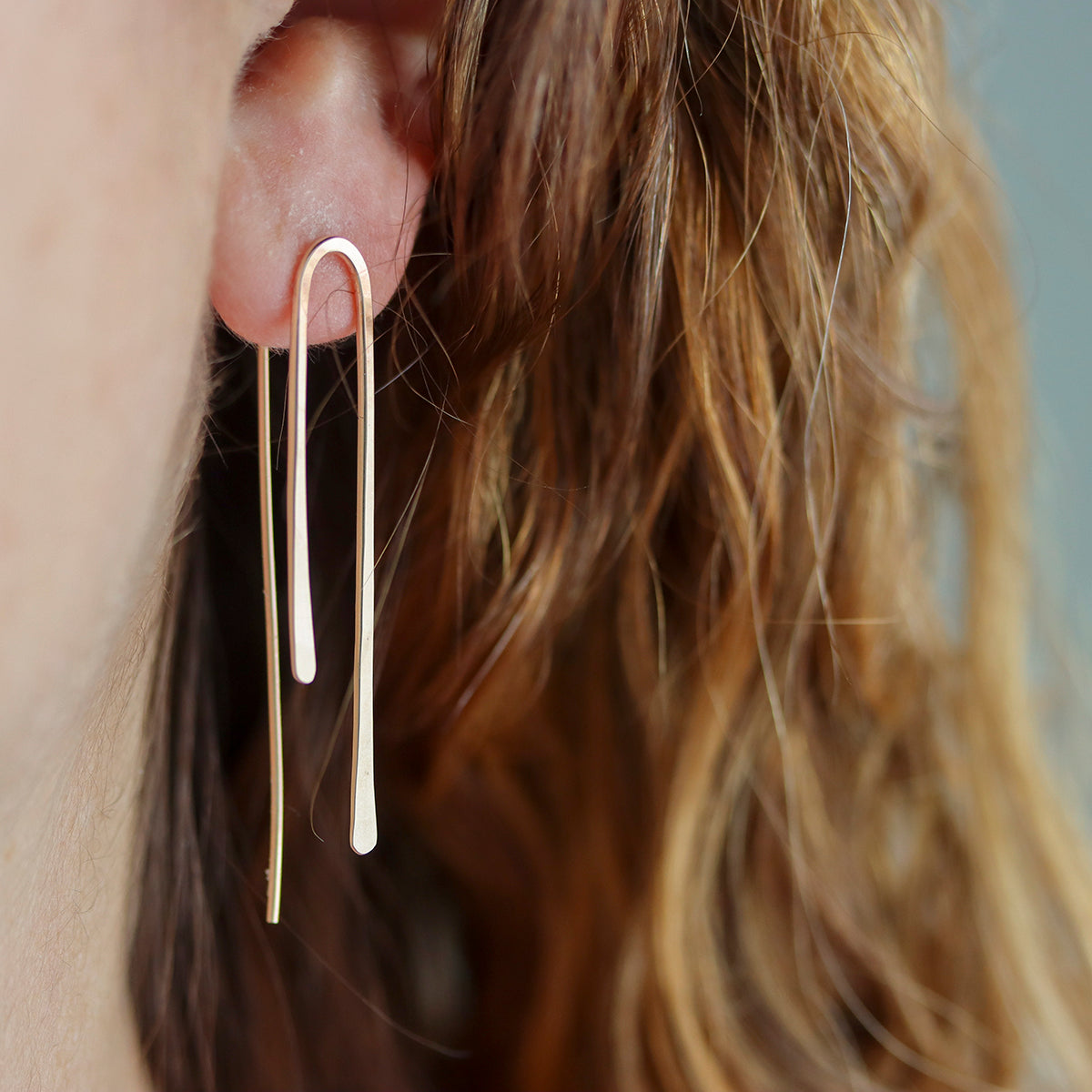 Gold earrings worn by a person with long hair, close-up of ear.