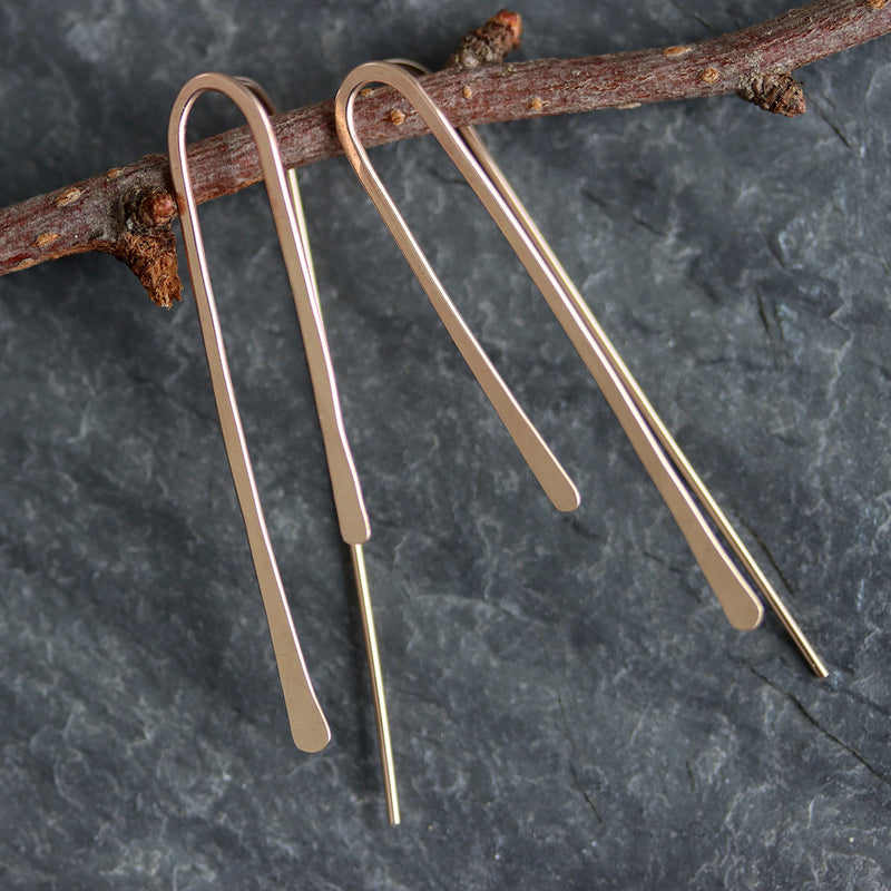 Pair of contemporary gold earrings hanging on a branch against a dark background