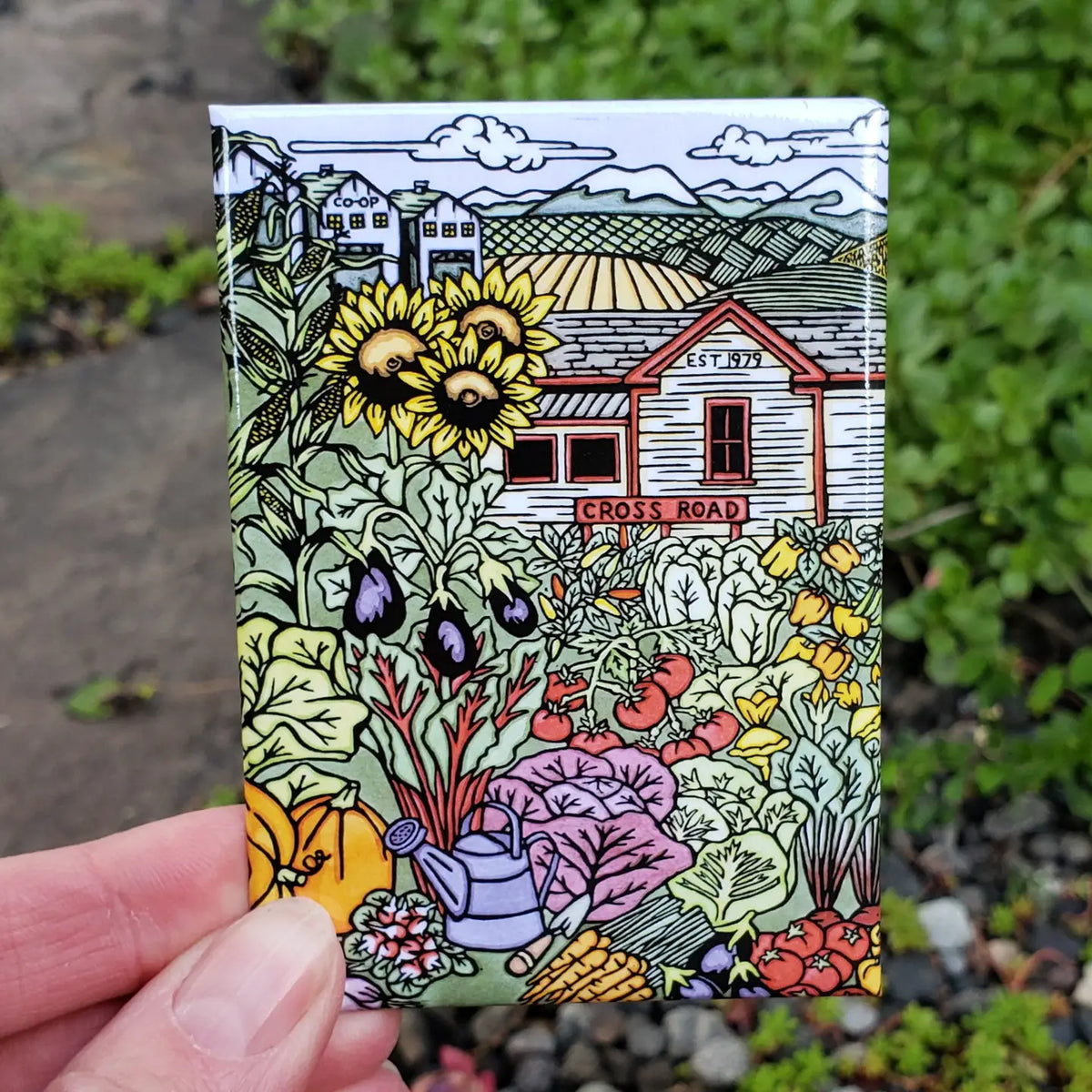 Colorful illustration of a house and garden on a small rectangular magnet held by a hand.