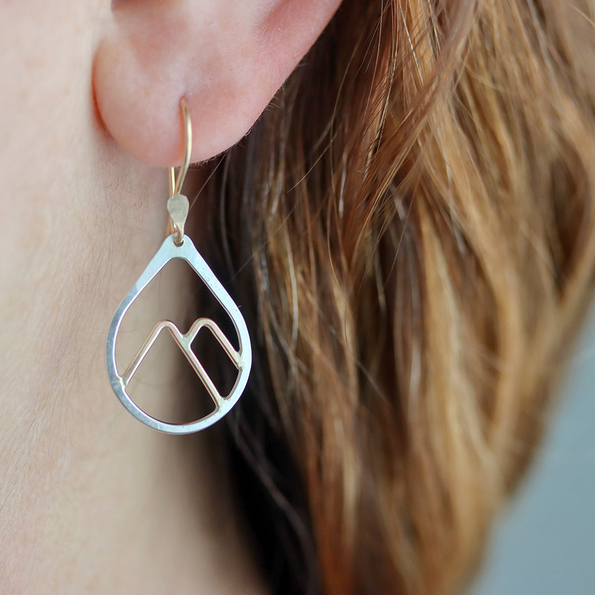 Silver mountain-shaped earrings worn by a person with blonde hair.