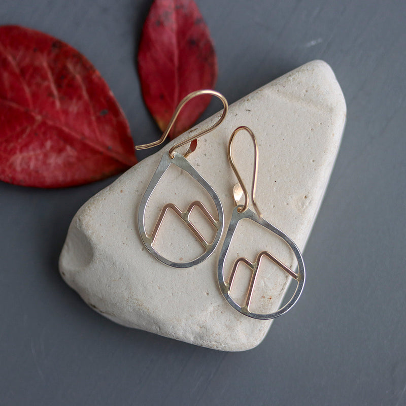 Pair of gold earrings on a stone with red leaves in the background