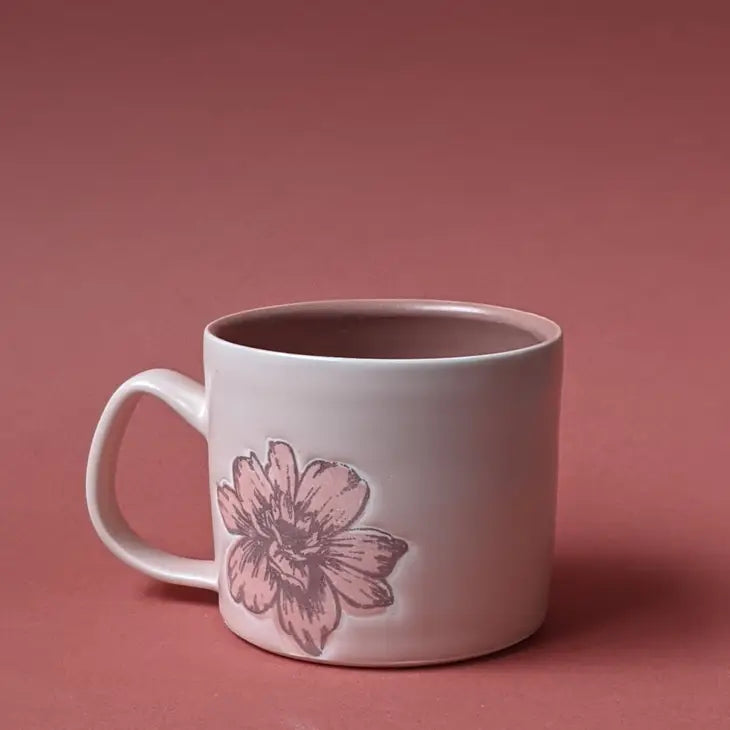 Handthrown mug on rose colored background, mug is  a light pink with a dusty rose flower