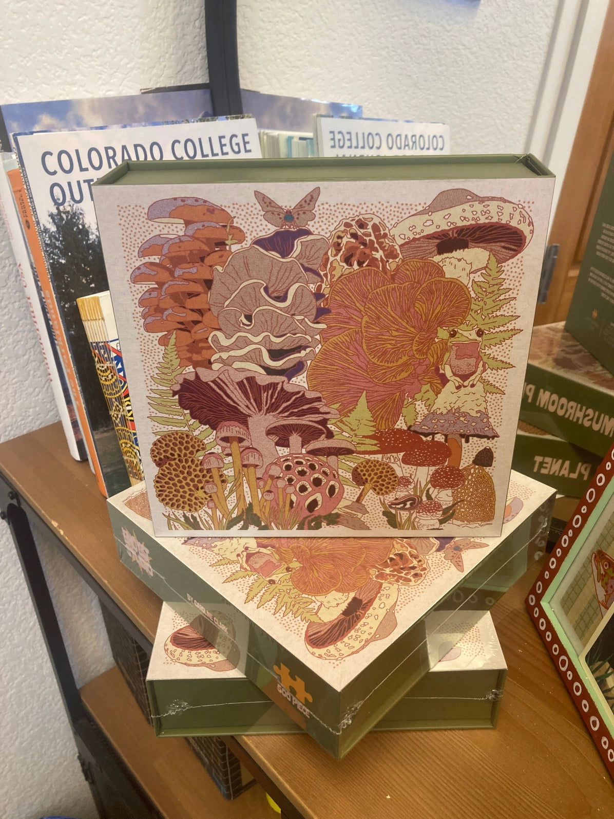 Stack of puzzles with a decorative cover featuring nature-themed illustrations on a wooden surface.