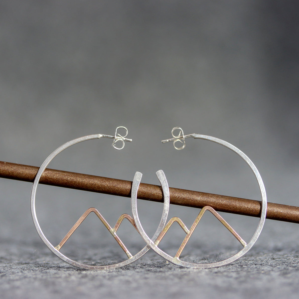 Silver hoop earrings with mountain designs on a gray background