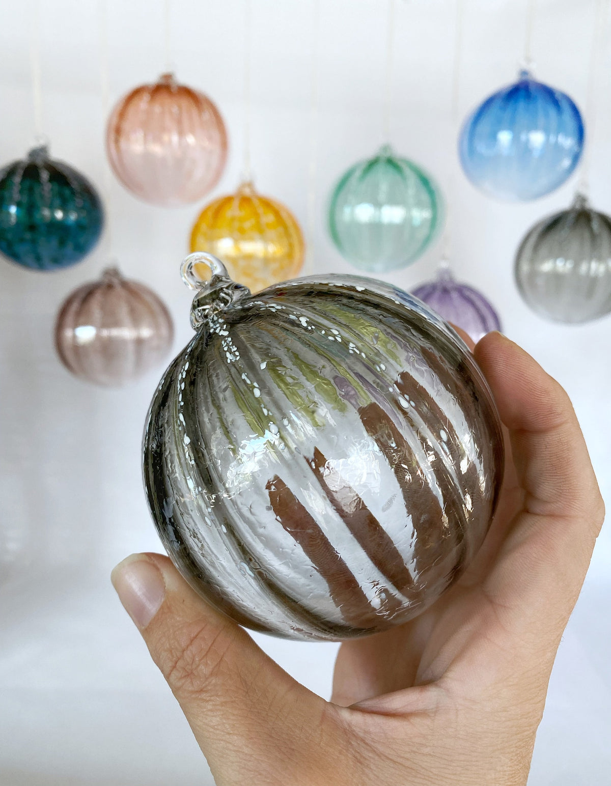 Hand holding a striped glass ornament with other colorful ornaments in the background.