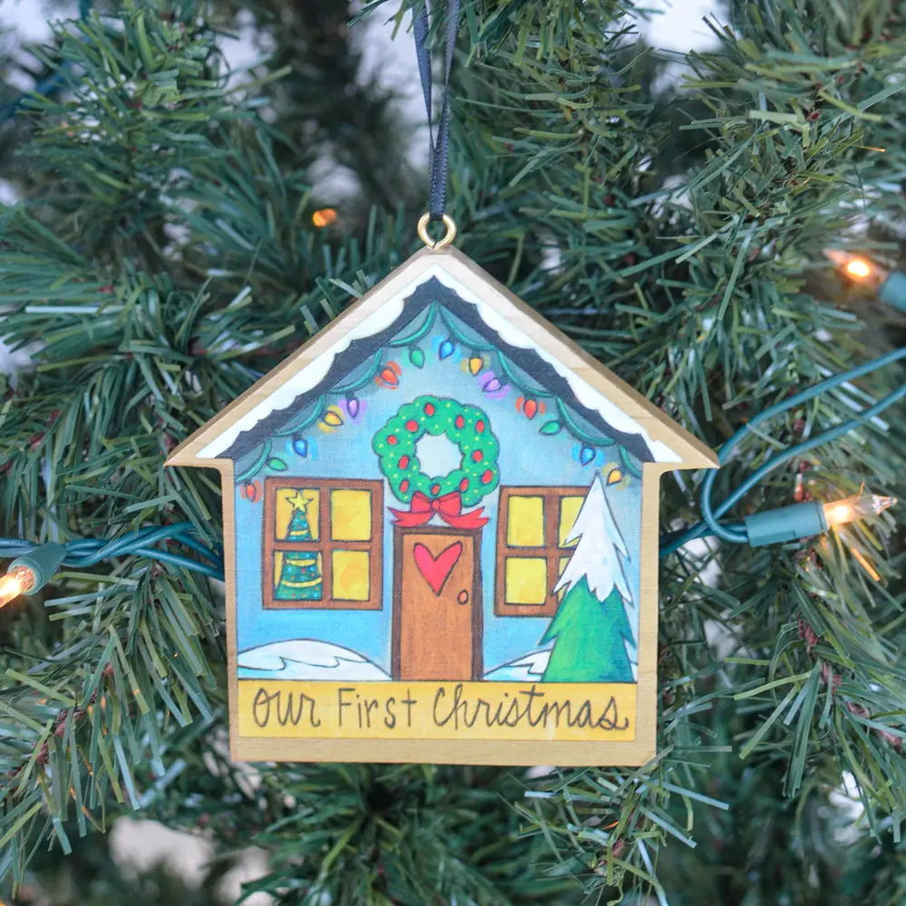Decorative house ornament with 'Our First Christmas' text on a Christmas tree.