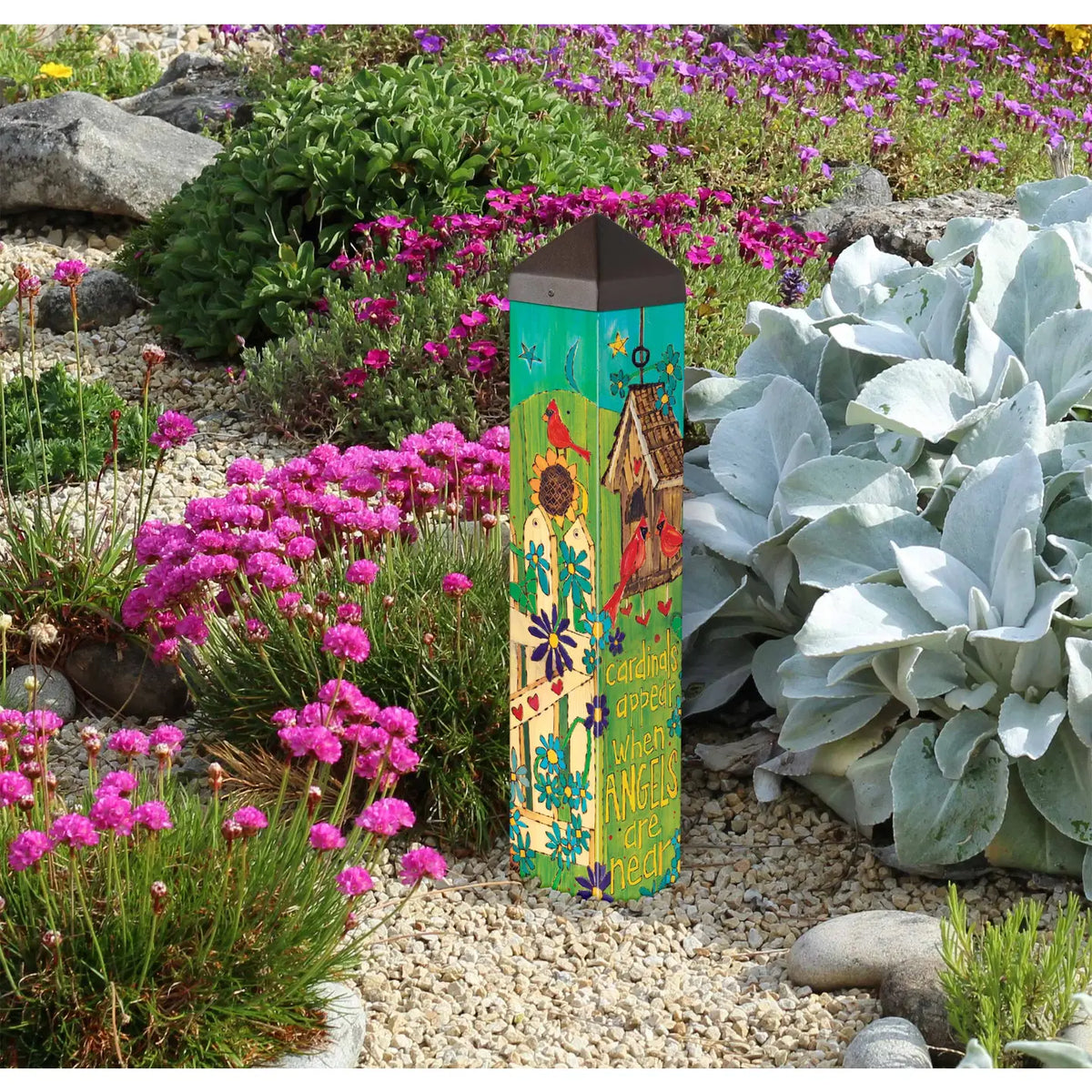 Decorative garden post with colorful design surrounded by flowers and plants