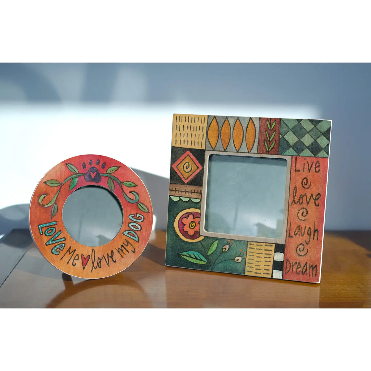 Two decorative picture frames on a reflective surface with a blurred background