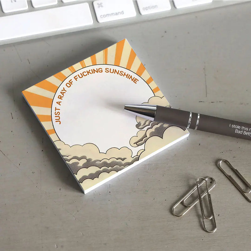 Notebook with cloud and sun design on a desk with a pen and paper clips.