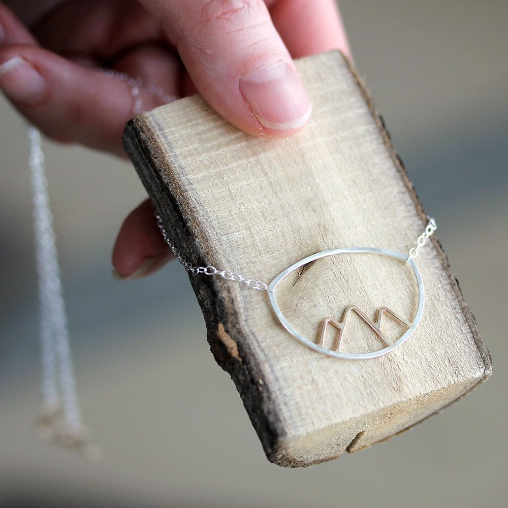 Silver necklace with a mountain design on a wooden block