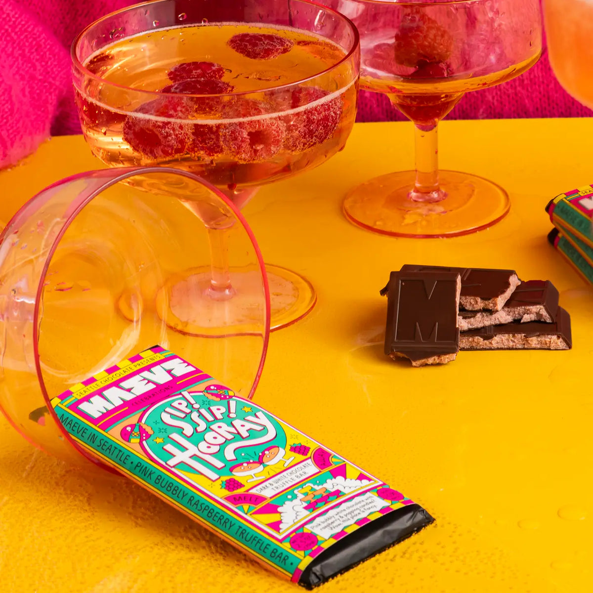 Cocktails with raspberries, chocolate bars, and a colorful candy bar on a yellow surface.