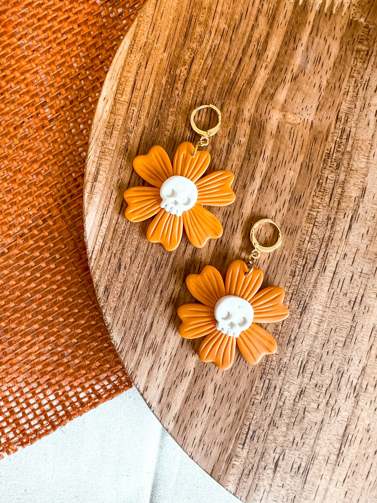 Polymer Clay Earrings in the shape of an orange flower with a white skull center and golden huggie hoops