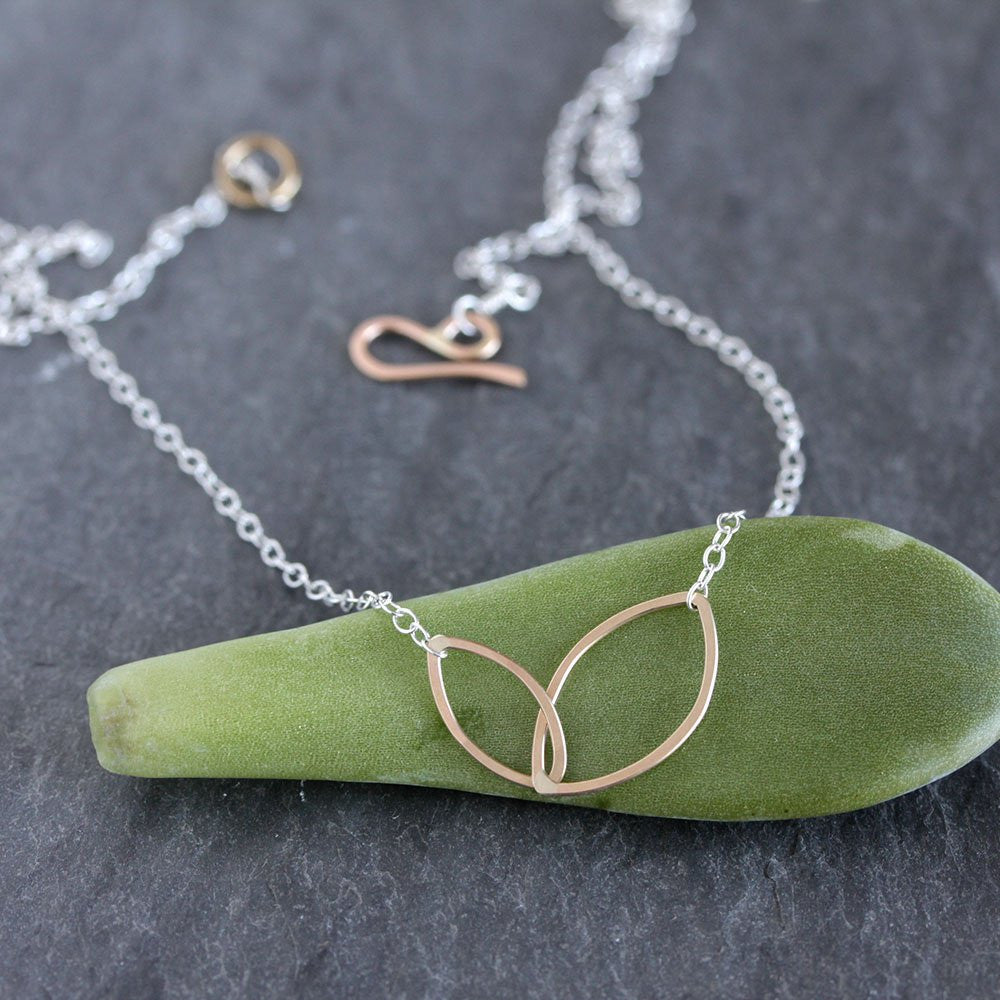 Gold necklace with a leaf-shaped pendant on a green stone against a dark background