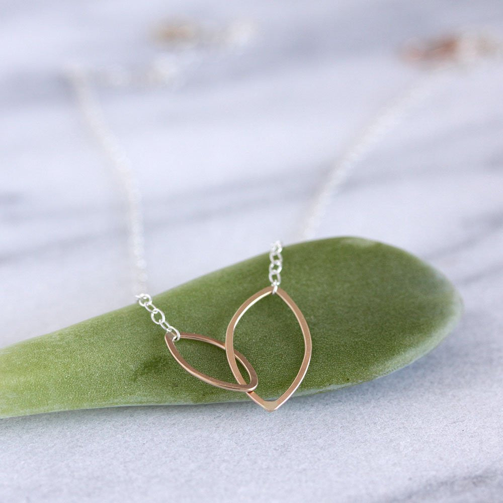 Silver + gold necklace with a leaf design on a green cushion against a light background