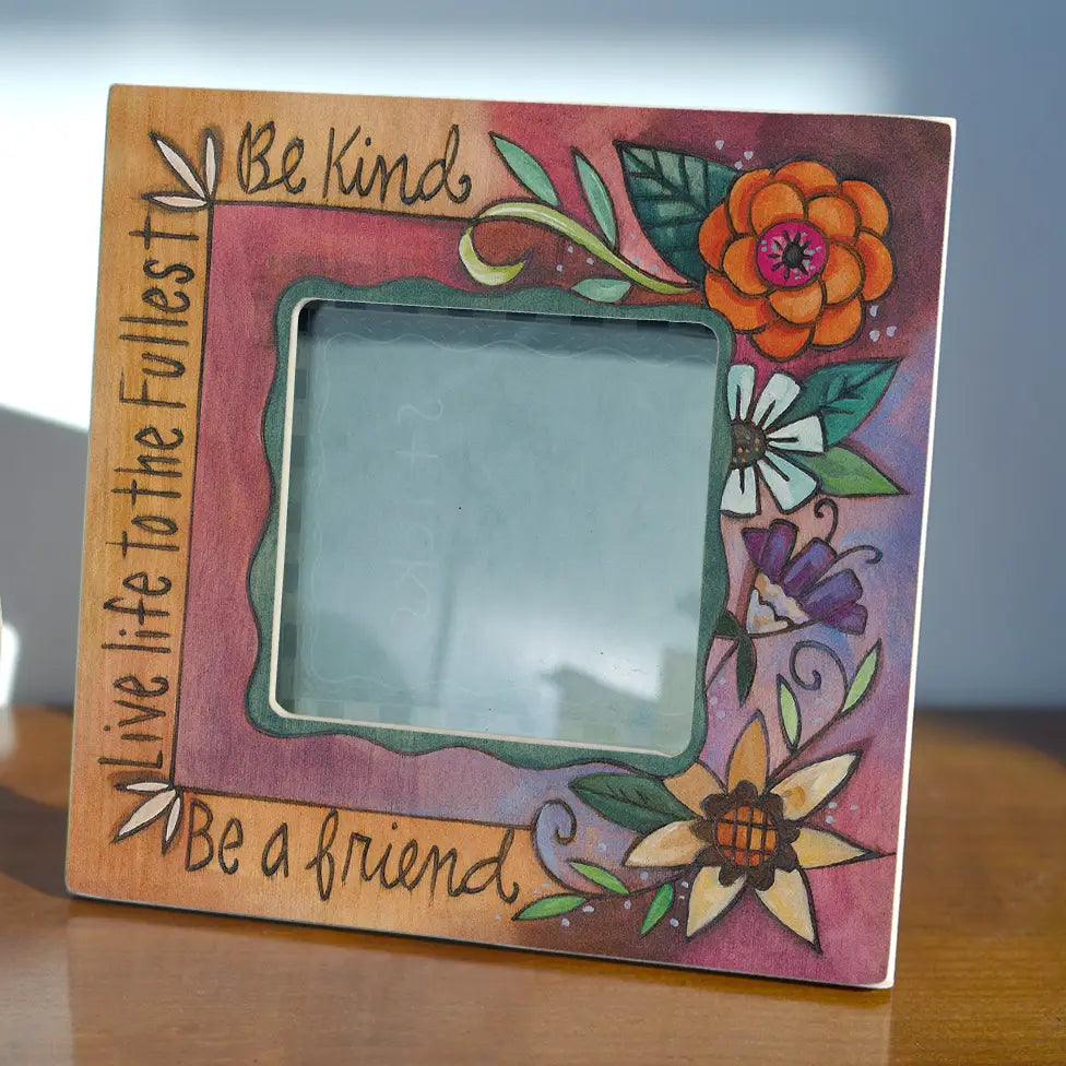 Decorative picture frame with floral designs and motivational text on a wooden surface.